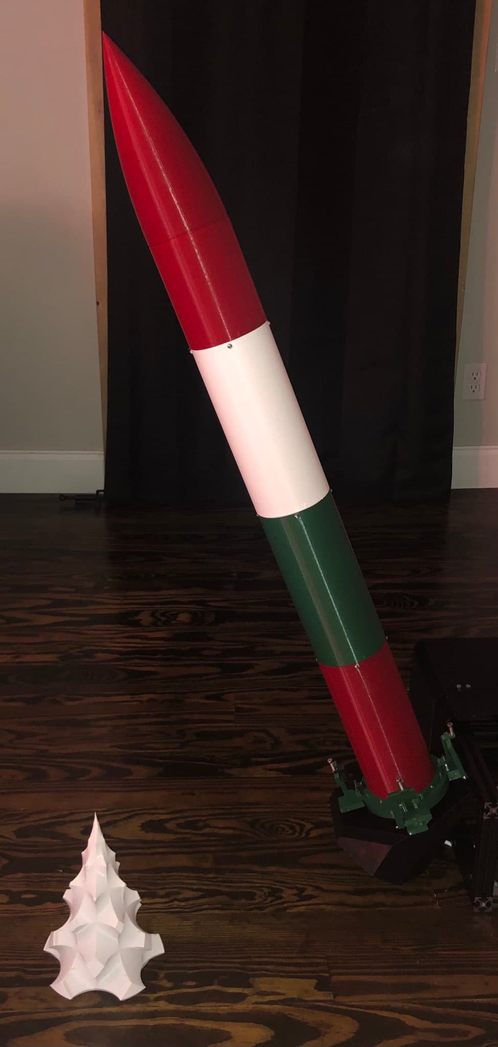 The Christmas rocket on the shop floor: red, white, and green airframe with a TVC fin can.