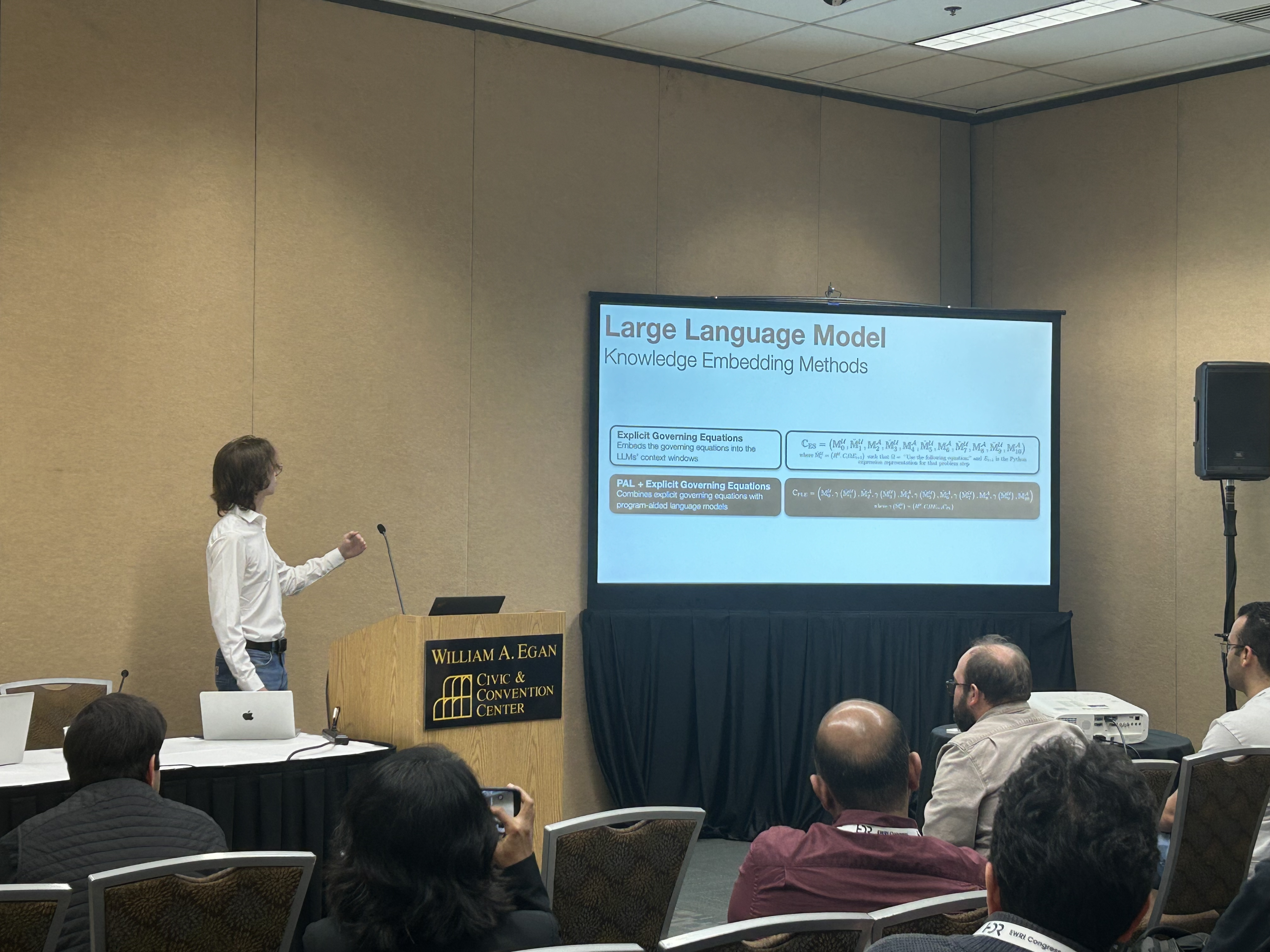 Presenting LLM knowledge-embedding methods at EWRI Congress 2025: podium, slide deck, and conference hall.