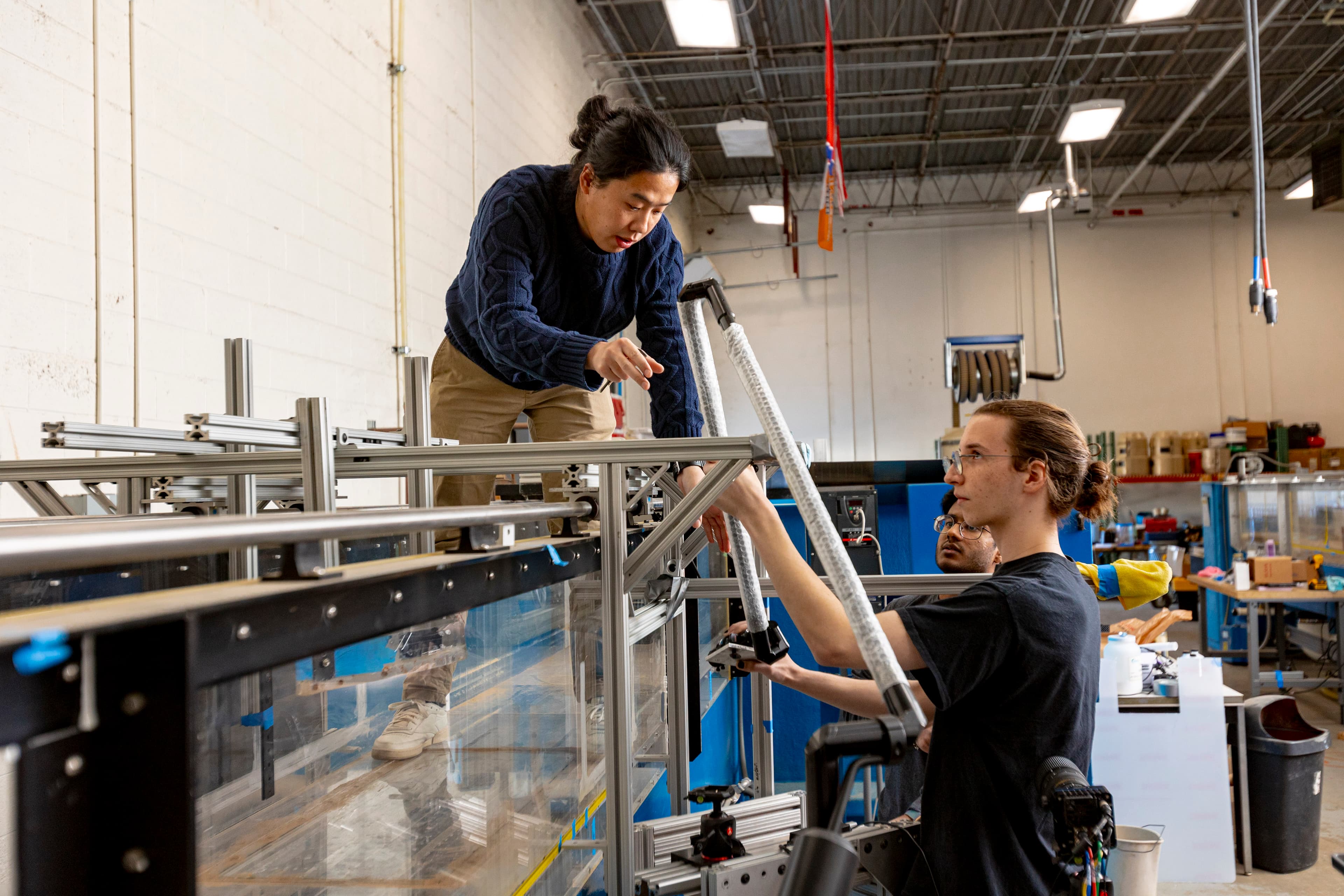 Lab team assembling a clear-channel flume: aluminum extrusions, glass walls, and hands on the frame.