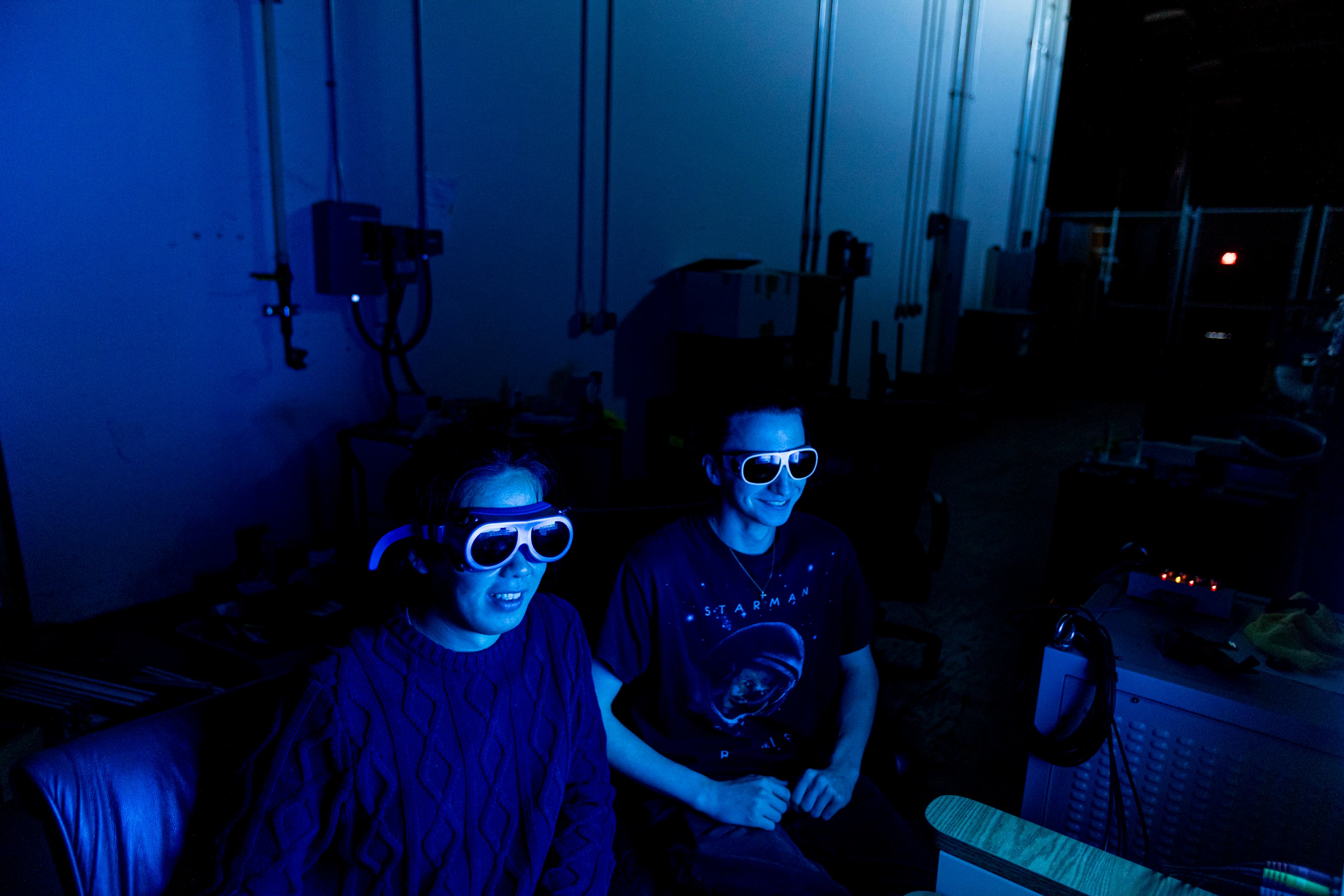 Two researchers in laser-safety goggles watching a flume run under blue light.