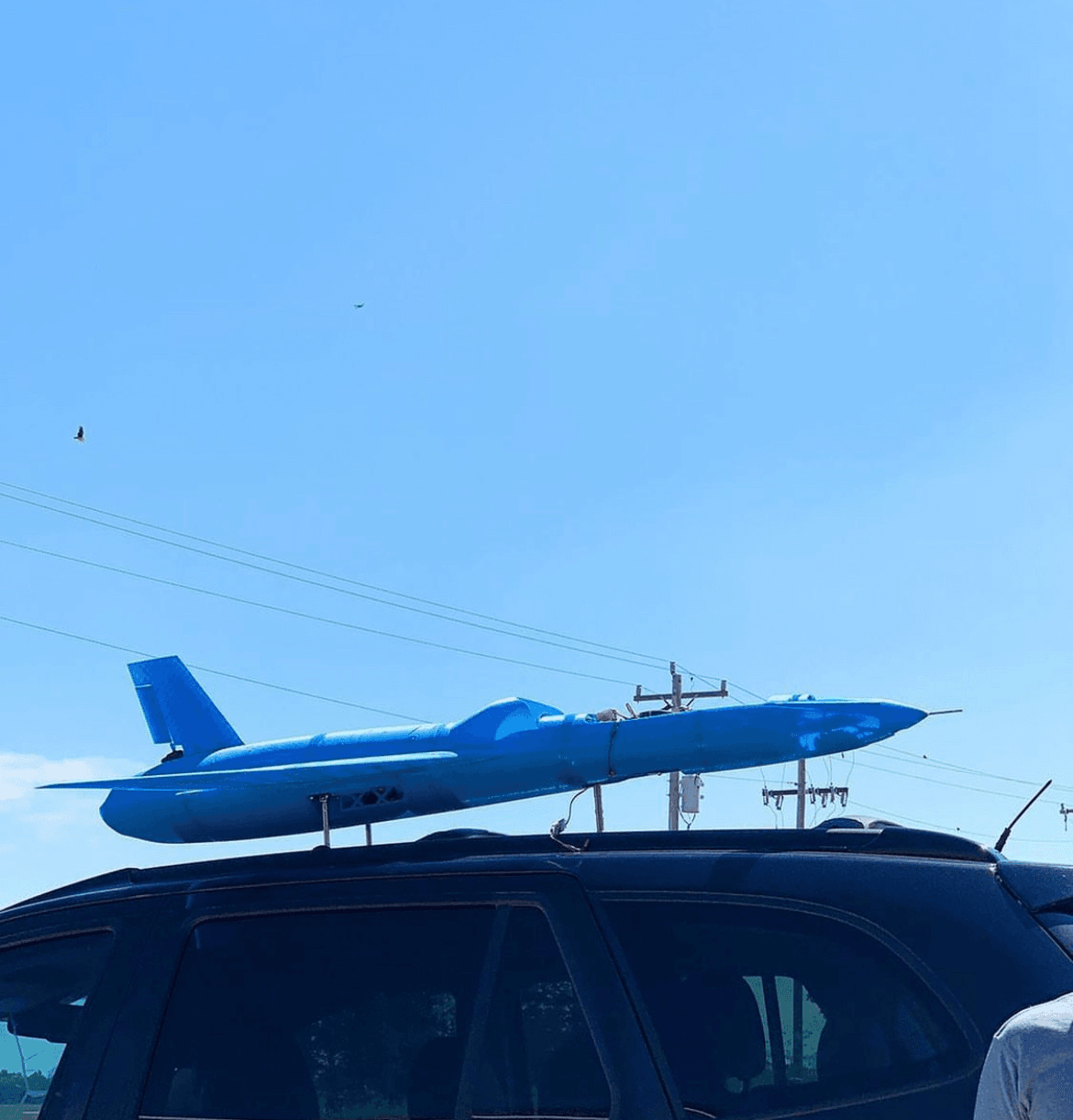 Project Boom aircraft strapped to a car roof under a clear sky.
